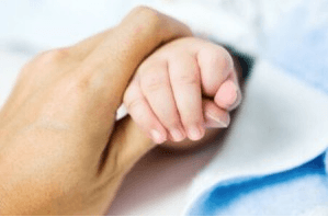 An adult holding baby's hand
